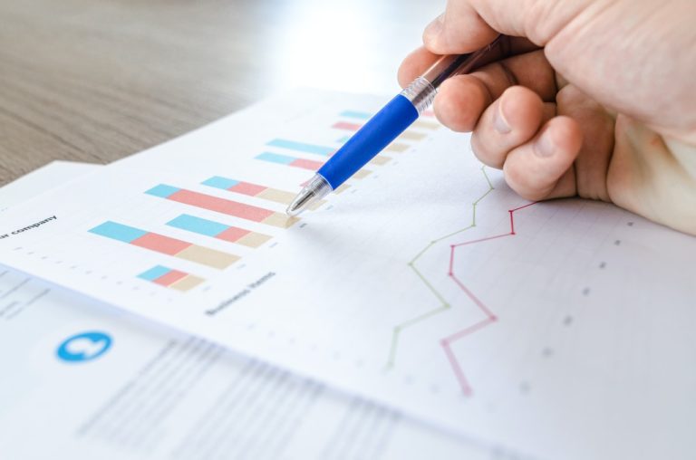 Hand holding blue pen pointing at graphs